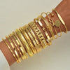 A stack of gold geometric minimalist bracelets worn on a wrist.