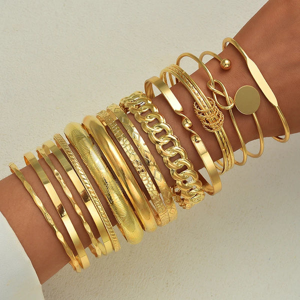 A stack of gold geometric minimalist bracelets worn on a wrist.
