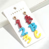 Un par de pendientes colgantes con forma de 1 y la letra B en tonos rojos, azules y amarillos.