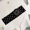 Black polka dot fabric headband with a round black button detail on a white background.