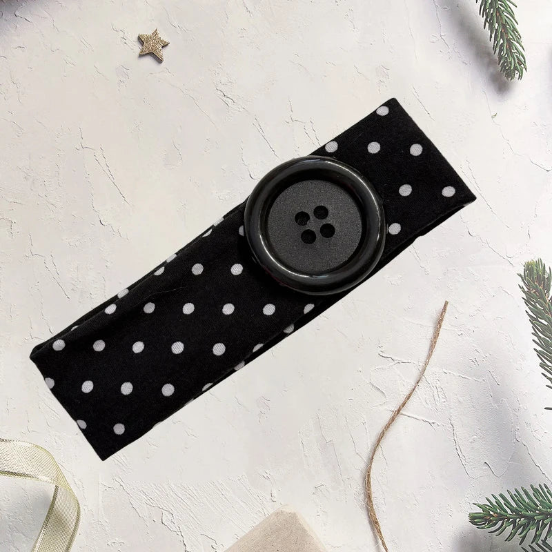 Black polka dot fabric headband with a round black button detail on a white background.