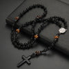 A black obsidian and tiger's eye beaded cross pendant necklace for men displayed on a dark surface.