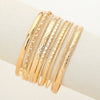 A stack of elegant gold hexagon star twist bangles worn on a wrist.