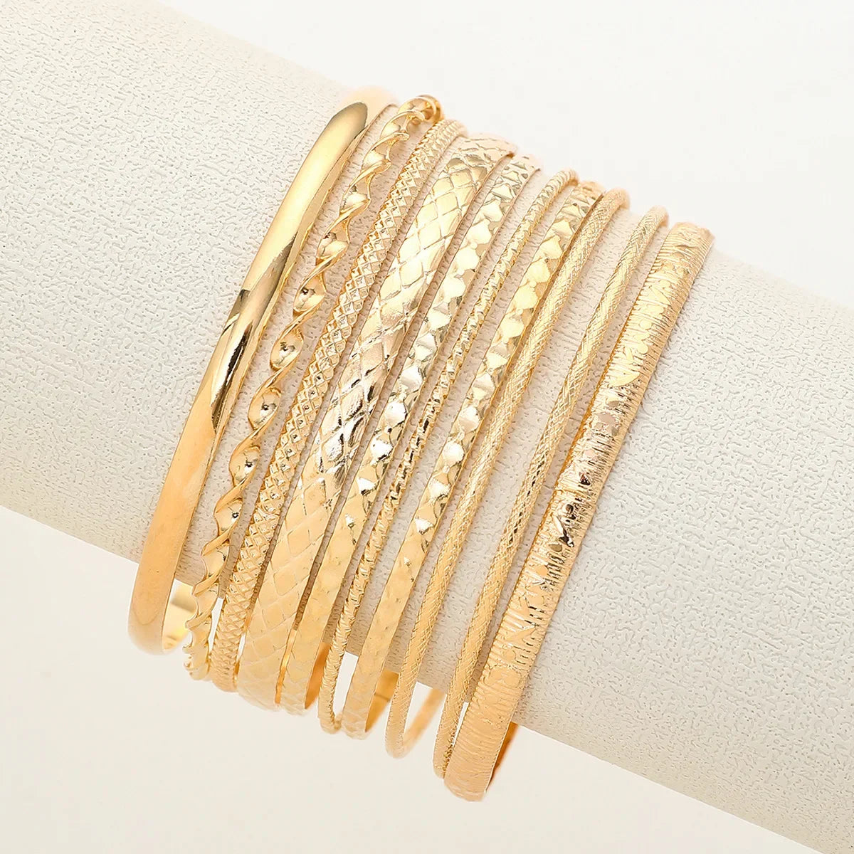 A stack of elegant gold hexagon star twist bangles worn on a wrist.