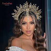 A close-up of a model wearing a gold rhinestone bridal crown headband with long dangling chains and dark brown wavy hair.