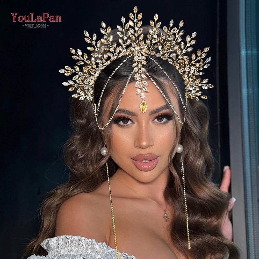 A close-up of a model wearing a gold rhinestone bridal crown headband with long dangling chains and dark brown wavy hair.
