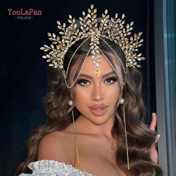 A close-up of a model wearing a gold rhinestone bridal crown headband with long dangling chains and dark brown wavy hair.