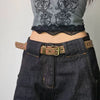 A close-up of dark denim jeans and a gray sheer top with black lace trim, featuring a brown belt with bronze rivets.