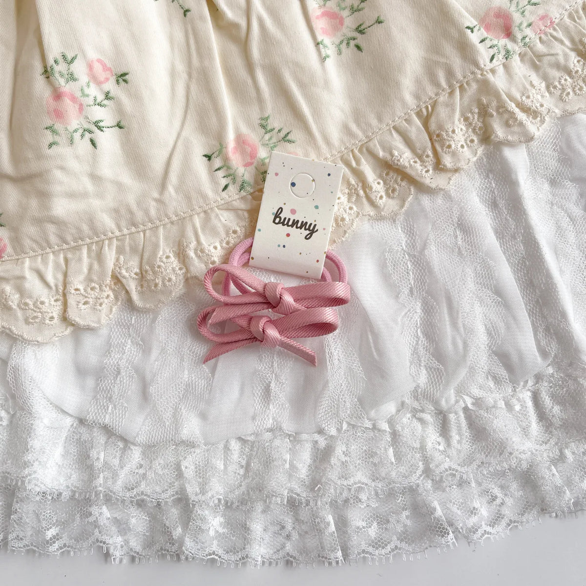 Un set de pinces à cheveux en nœud rose avec un charm de lapin sur un tissu en dentelle blanche.