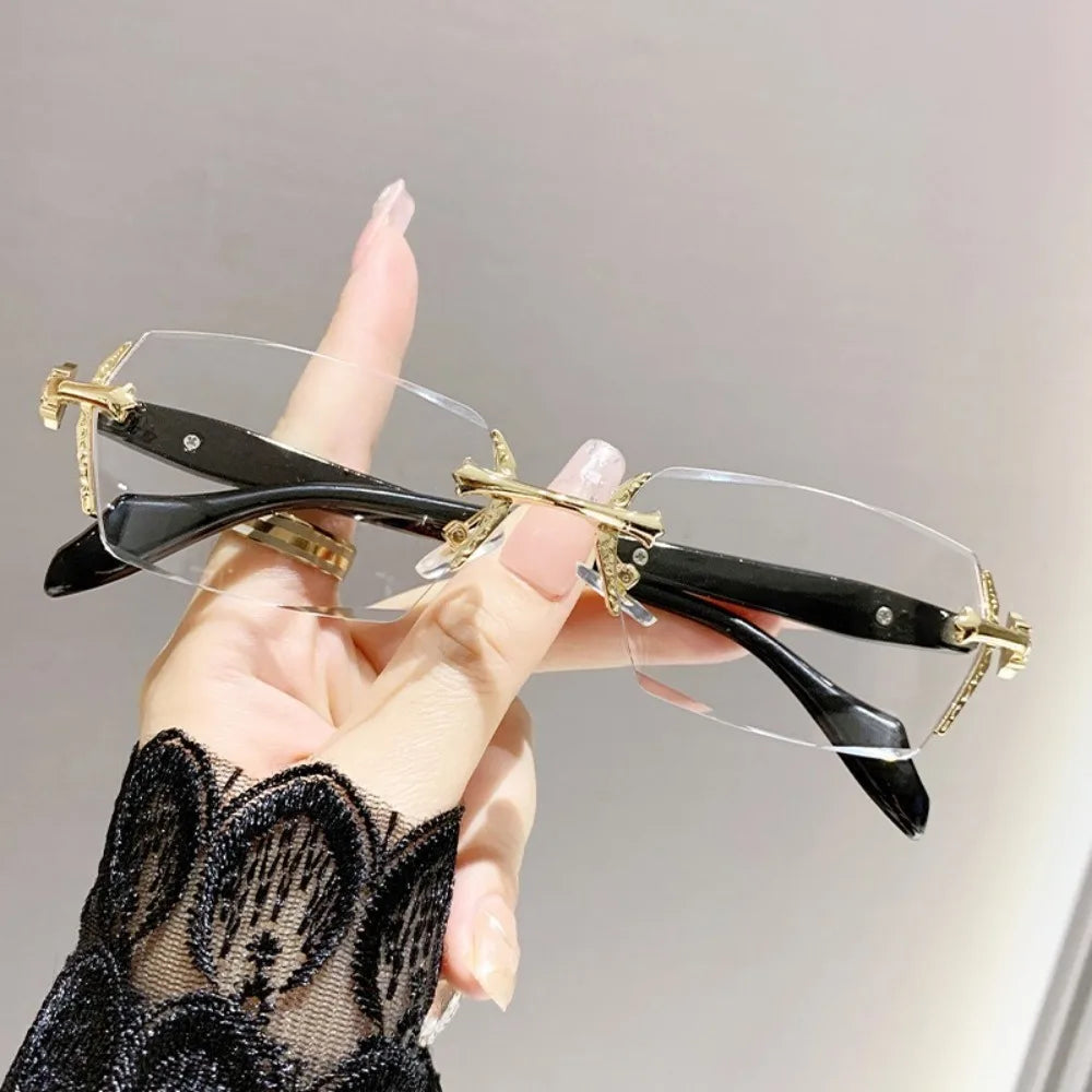 A hand holds a pair of vintage Y2K frameless glasses with gold accents and clear lenses against a light background.