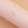 Un anklet argenté à perles délicat avec un charm en forme de cœur sur le poignet d'une personne.