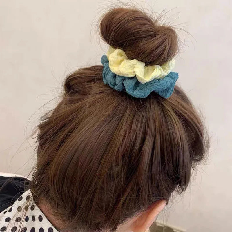 A close-up of a person's hair styled in a bun with a blue and yellow knitted scrunchie headband.
