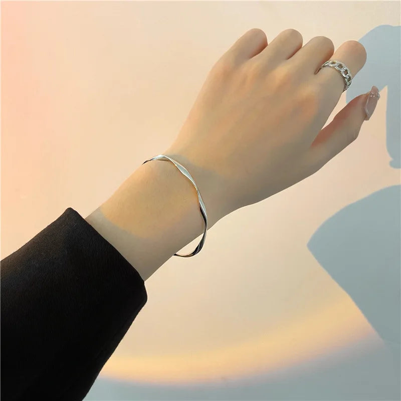 A hand wearing a silver twisted wave cuff bracelet on the wrist against a soft, bright background.