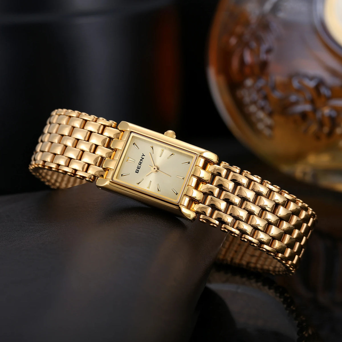 Gros plan d'une montre quartz pour femme plaquée or, avec un cadran rectangulaire et un bracelet métallique texturé.