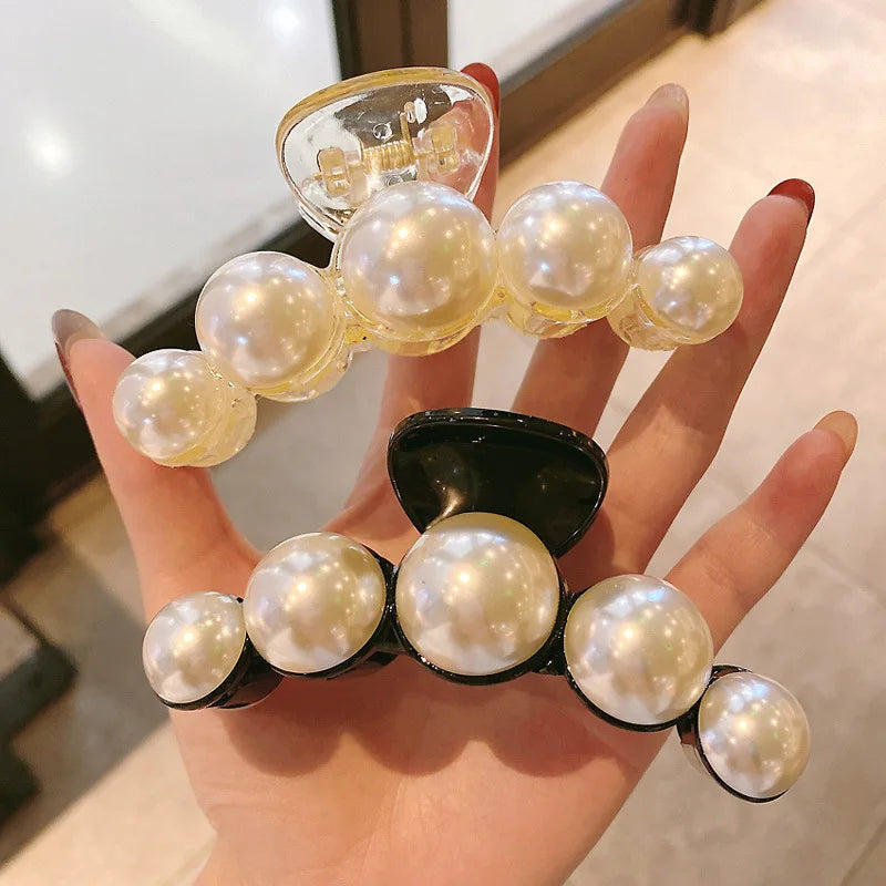 A hand holds a set of simulated pearl hair claws, featuring round pearls on a gold-toned base.