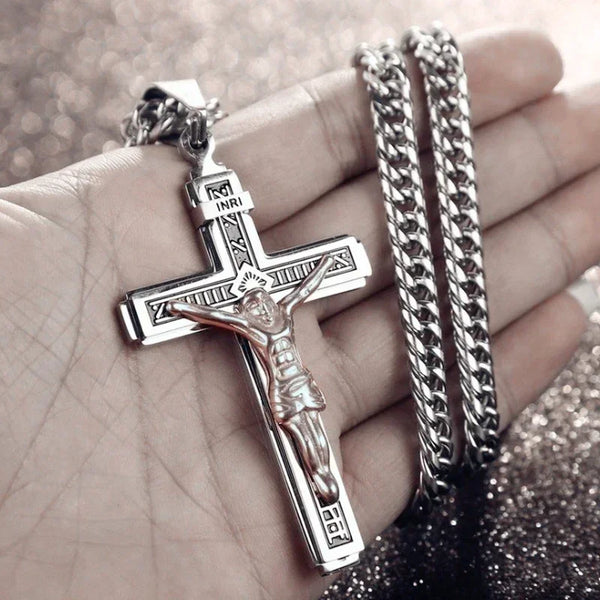 A silver cross amulet necklace with a figure of Christ and two silver chain bracelets is held in a hand.