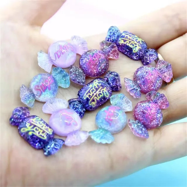 A set of 10 purple and blue resin nail art charms displayed on a person's hand.