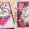A pink and white floral print silk scarf tied in a bow, displayed on a black surface.