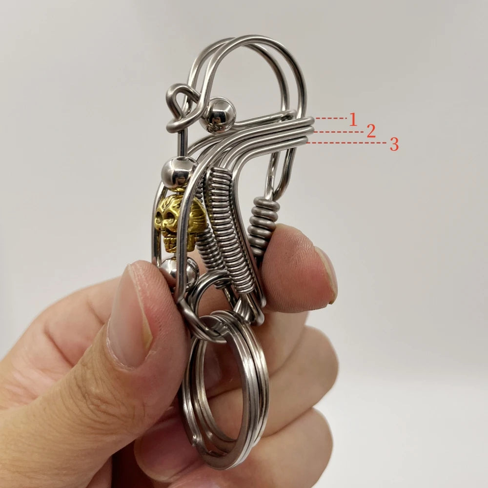 Un porte-clés mécanique en acier inoxydable avec des ressorts enroulés et un petit charm en laiton tenu dans une main.