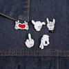 A close-up of a dark denim fabric featuring white enamel pins depicting various finger gestures and a heart.