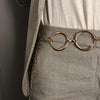 Cadena de metal dorada como cinturón puesta sobre pantalones de lino gris claro.