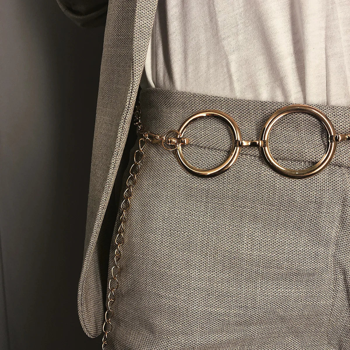 Cadena de metal dorada como cinturón puesta sobre pantalones de lino gris claro.