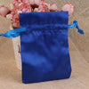 A royal blue satin drawstring pouch with a light blue ribbon, set against a background of pink flowers.