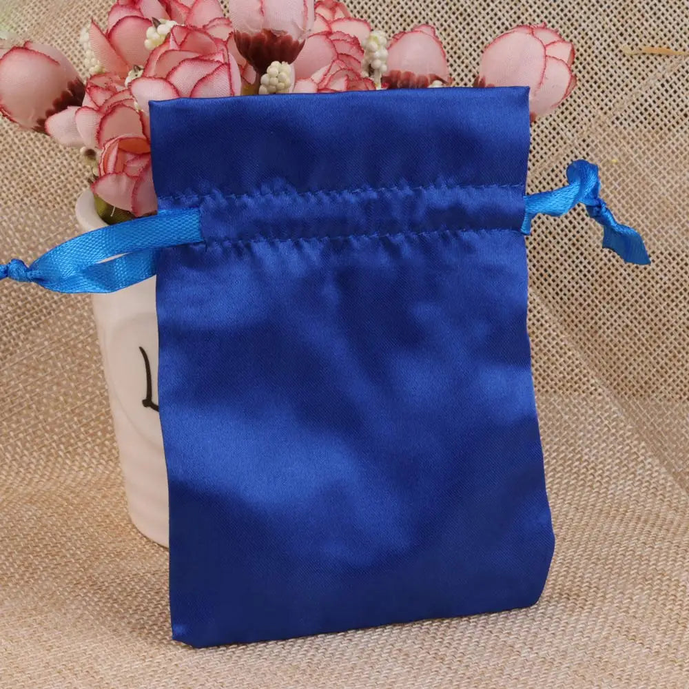 A royal blue satin drawstring pouch with a light blue ribbon, set against a background of pink flowers.