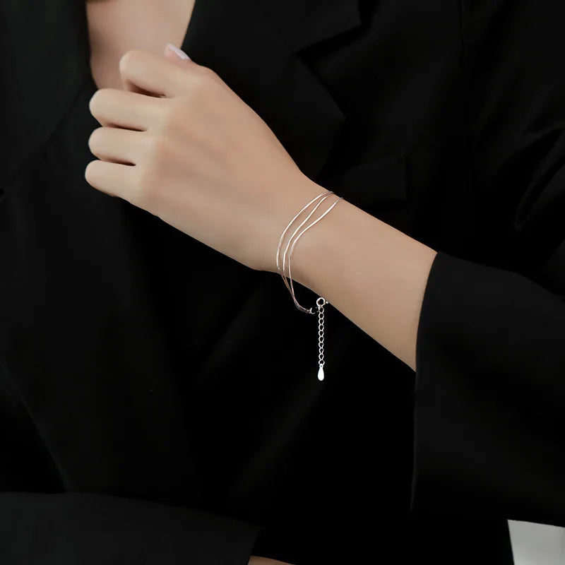 A close-up of a woman's wrist wearing a sterling silver double heart charm bracelet under a black blazer.