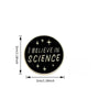 A round black lapel pin with the text I BELIEVE IN SCIENCE engraved in gold.