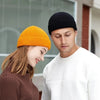 A young couple smiling while wearing warm knitted beanie caps, one orange and one black.