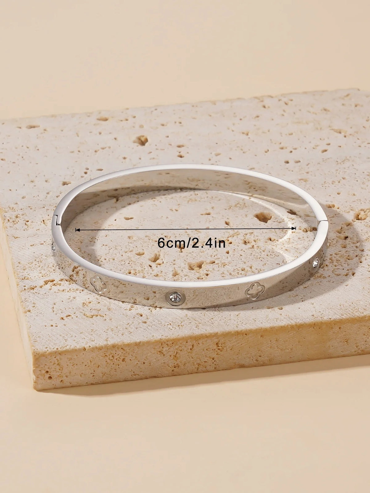 A silver stainless steel bangle bracelet is displayed on a light beige textured surface.