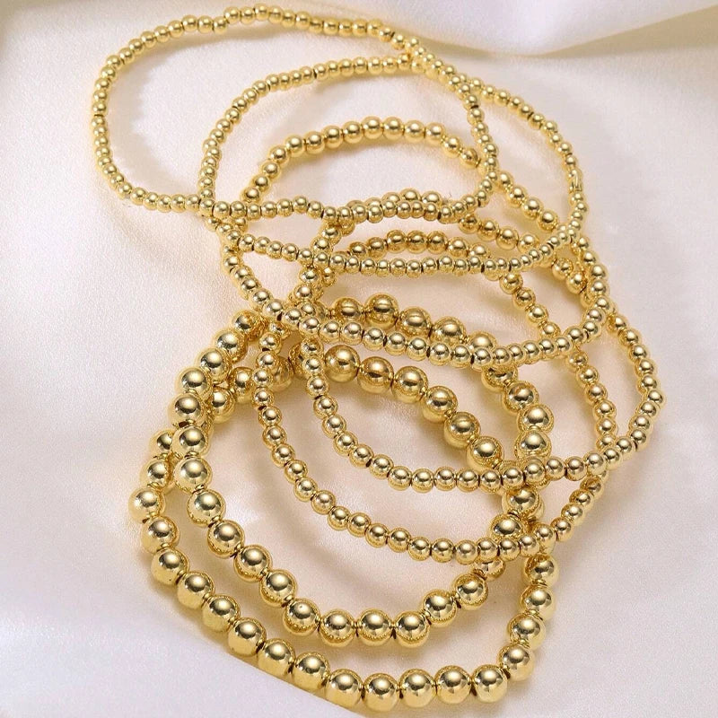 A set of minimalist round beaded bracelets in gold color arranged on a white background.
