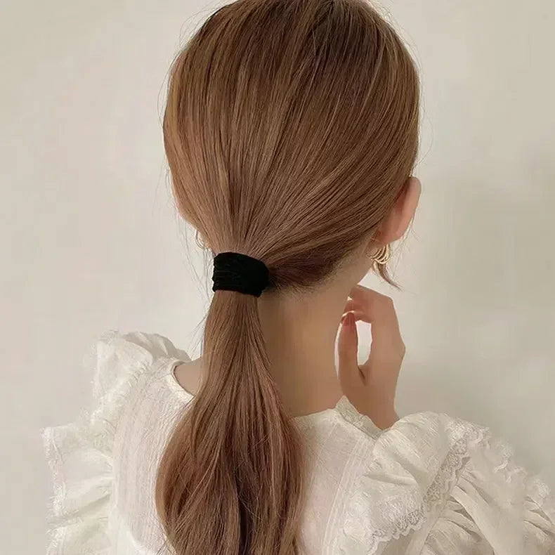 A woman with long, light brown hair tied in a ponytail using a black elastic hair band.