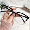A hand holds a pair of black-framed anti-blue light spectacles with clear lenses against a white marble background.