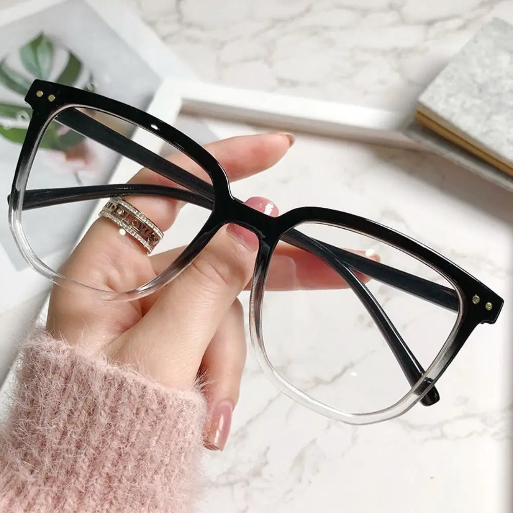 A hand holds a pair of black-framed anti-blue light spectacles with clear lenses against a white marble background.