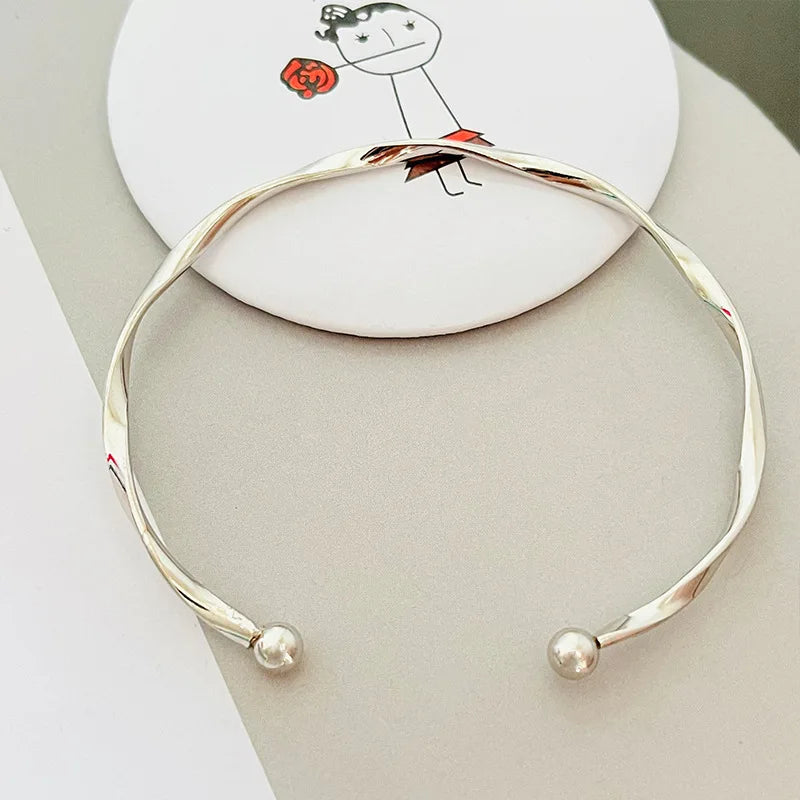 Silver twisted wave cuff bracelet worn on a white background with a hand-drawn illustration.