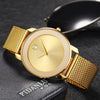 A gold-toned quartz wristwatch with a round face and mesh strap resting on a dark surface.