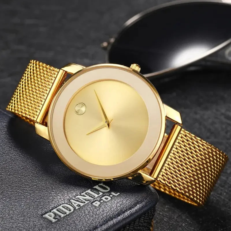 A gold-toned quartz wristwatch with a round face and mesh strap resting on a dark surface.