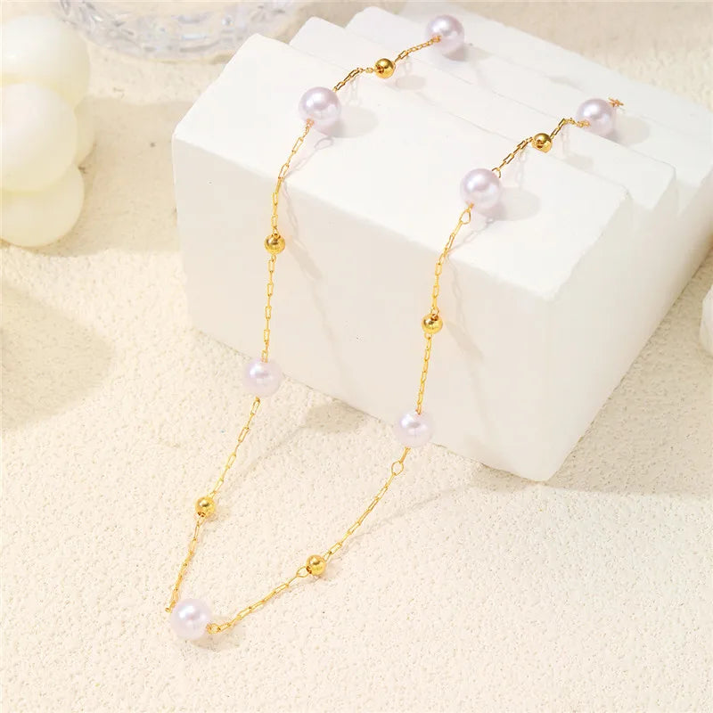 Un délicat collier en or avec de petites perles blanches rondes, présenté sur un bloc blanc.