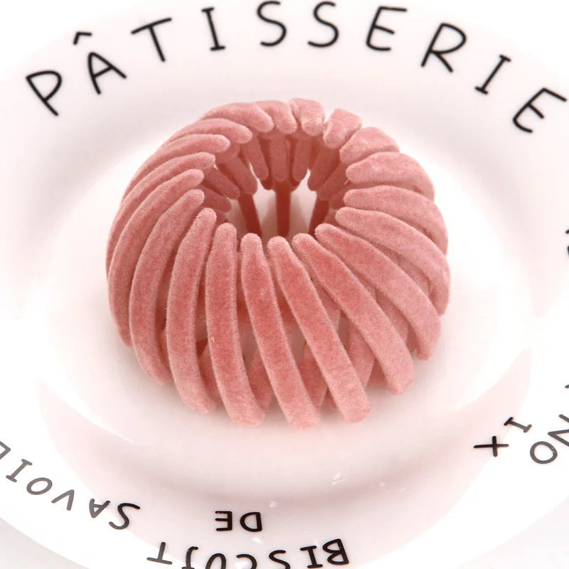 A pink, spiral-shaped hair clip is shown on a white plate with text around the rim.