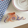 Pince à cheveux en forme d'octopus, orange et blanc translucide avec des pois bleus, posée sur une surface blanche.