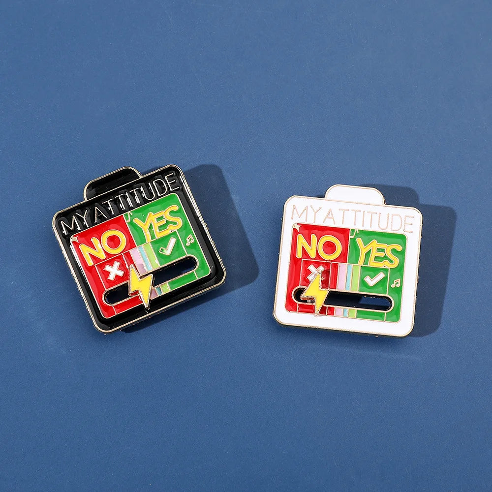 Two enamel brooch pins showing 'NO YES' and 'YES' mood expressions on a blue background.