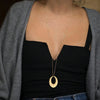 Nahaufnahme einer Frau mit einer goldenen Edelstahl-Arc-Halskette über einem schwarzen Top und einem grauen Cardigan.