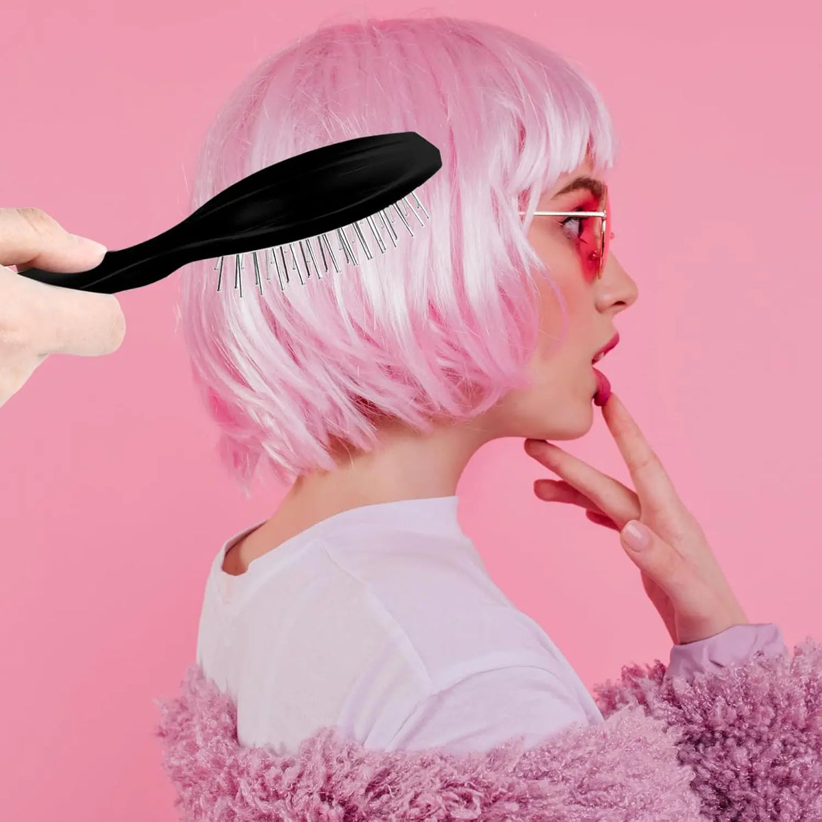 A woman with pink hair is shown using a black anti-static steel comb hair brush for wig grooming.
