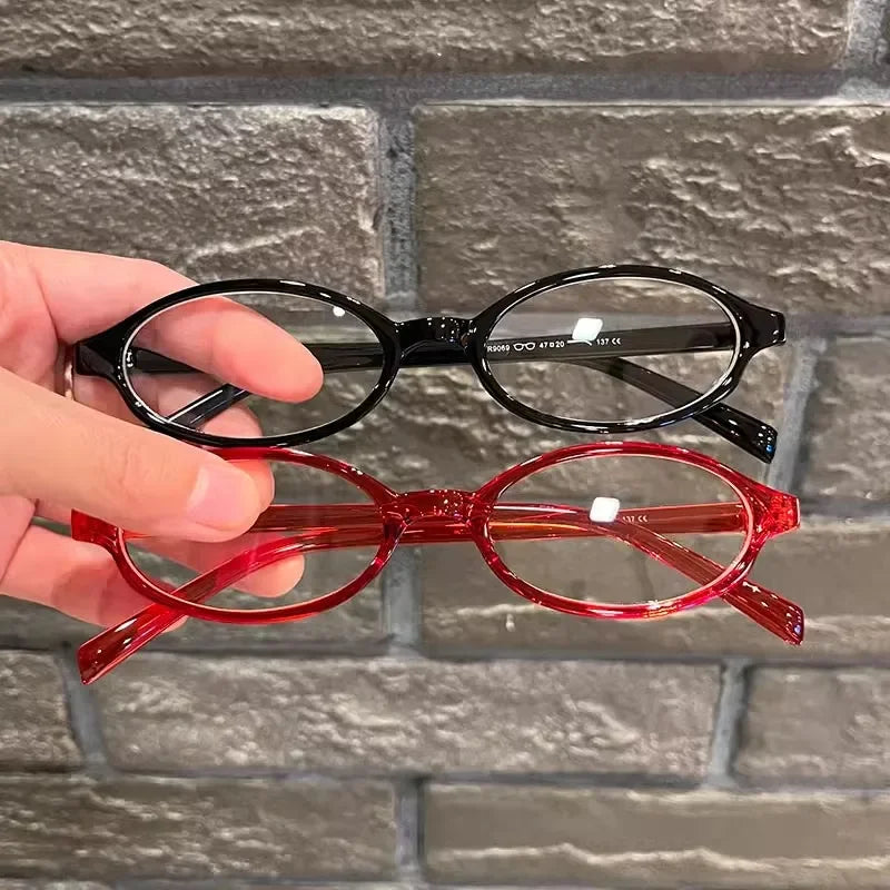 Une main tient une paire de lunettes de mode ovales rouges rétro sur un fond de briques grises.