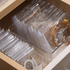 A clear plastic storage box filled with bulk packs of self-sealing jewelry pouches and rings.