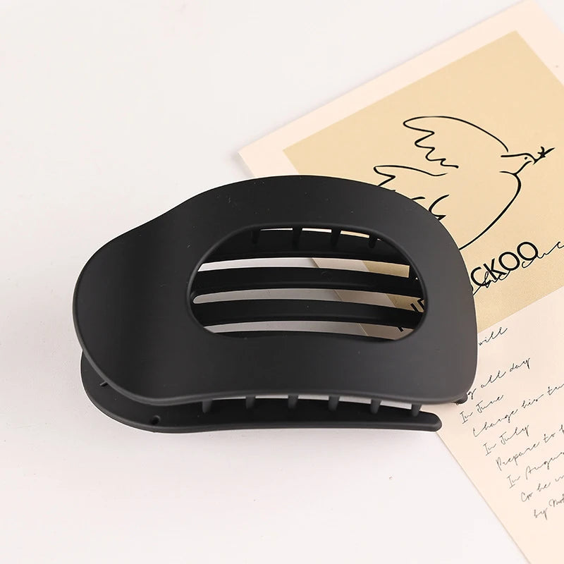 A black flat circular hair clip is shown next to a piece of paper with a line drawing of a bird.