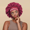 A woman wearing a deep magenta satin sleep bonnet with a Sagittarius wrap band.
