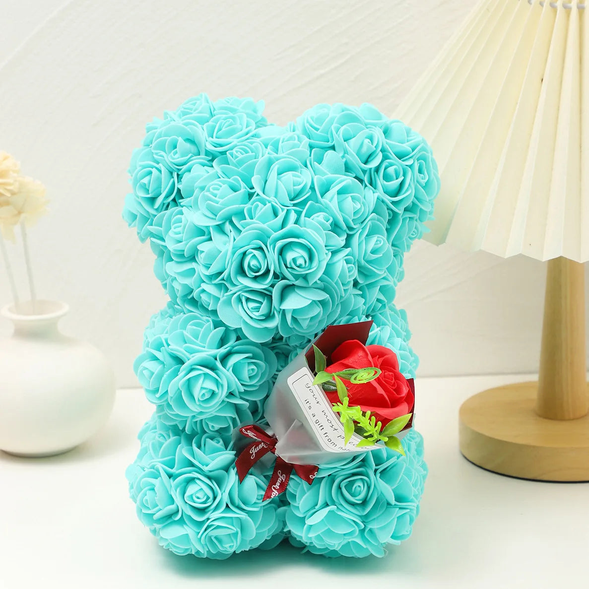 Un bouquet de roses en mousse bleu clair en forme de ours en peluche à côté d'une lampe de couleur crème.